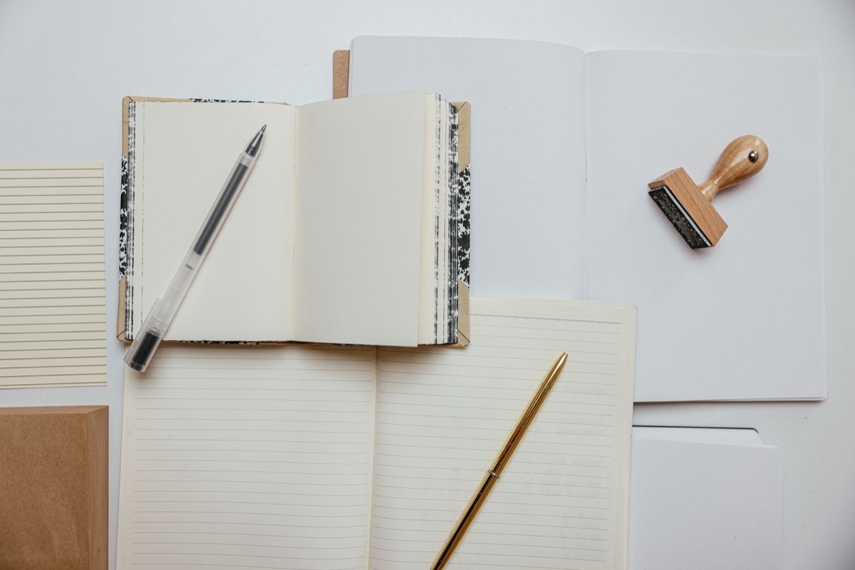 An open notebook, a pen and a wooden rubber stamp on a white desk