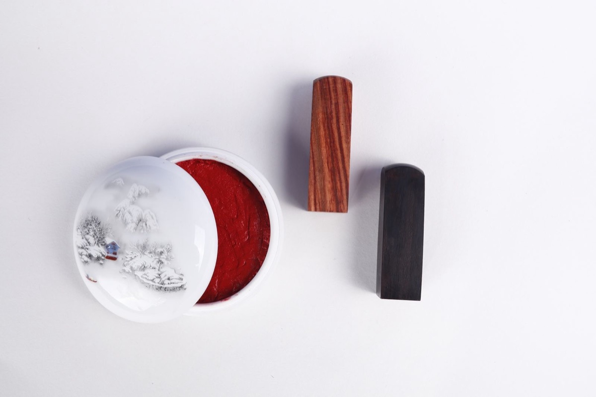 Two wooden seal stamps beside a dish of red ink on a white surface
