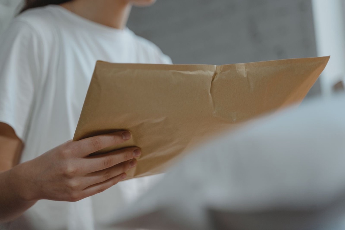 Hands holding a brown paper envelope, a person in a white T-shirt seen from the chest down