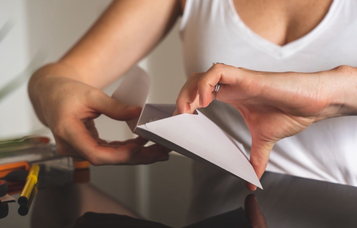 Hands opening a white envelope at a dark desk with markers beside it