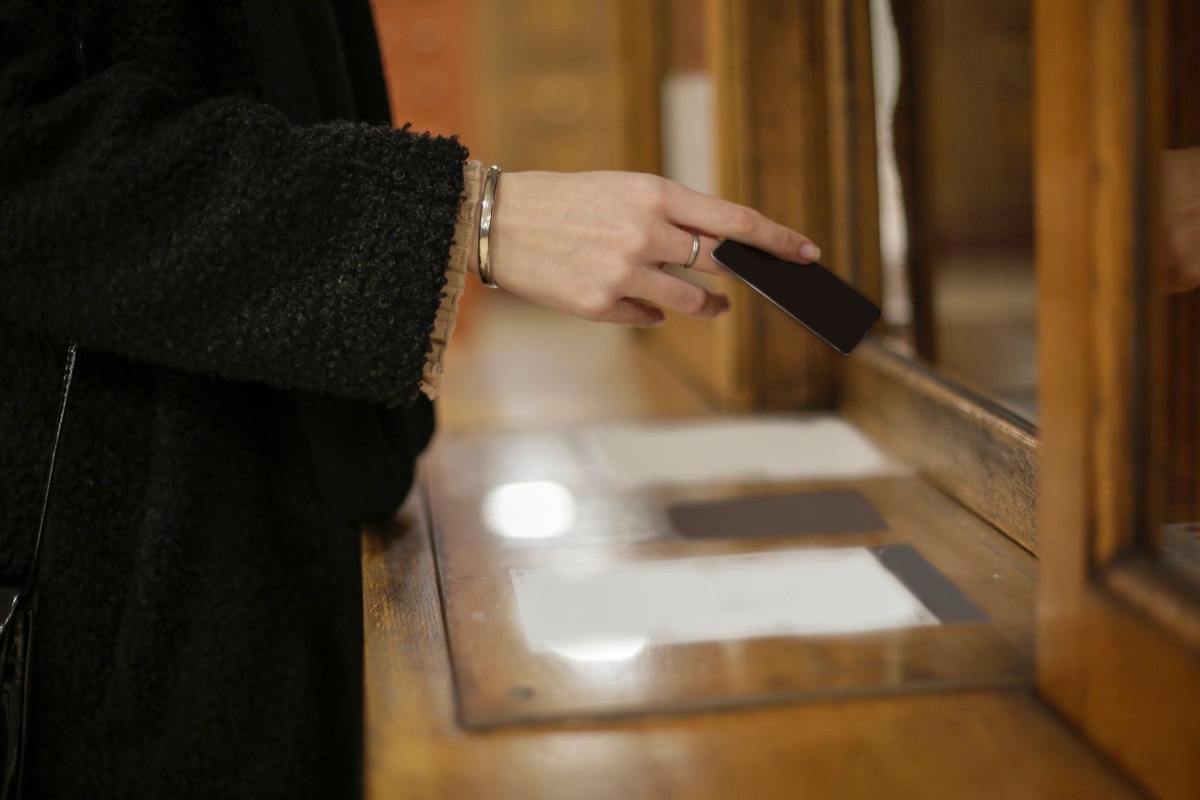 A woman's hand holding a small dark card at a wooden counter window