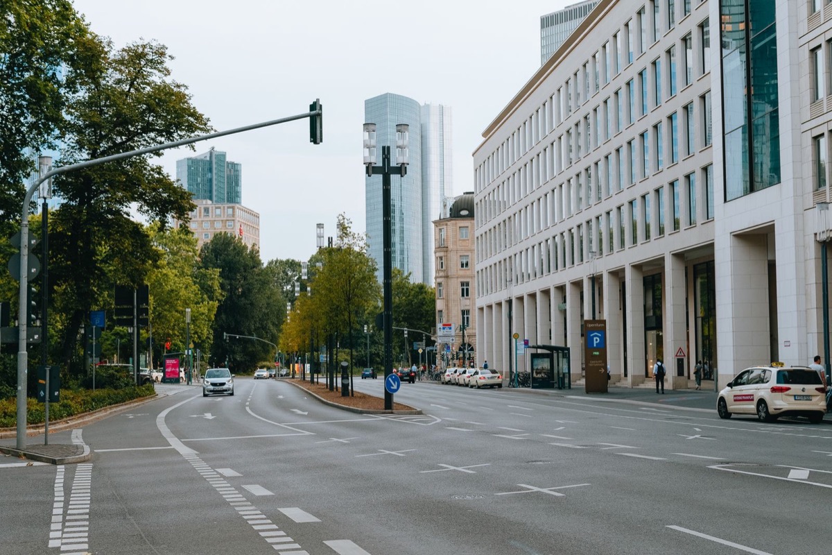 A wide city street with trees, a pale office building and a few cars in daylight