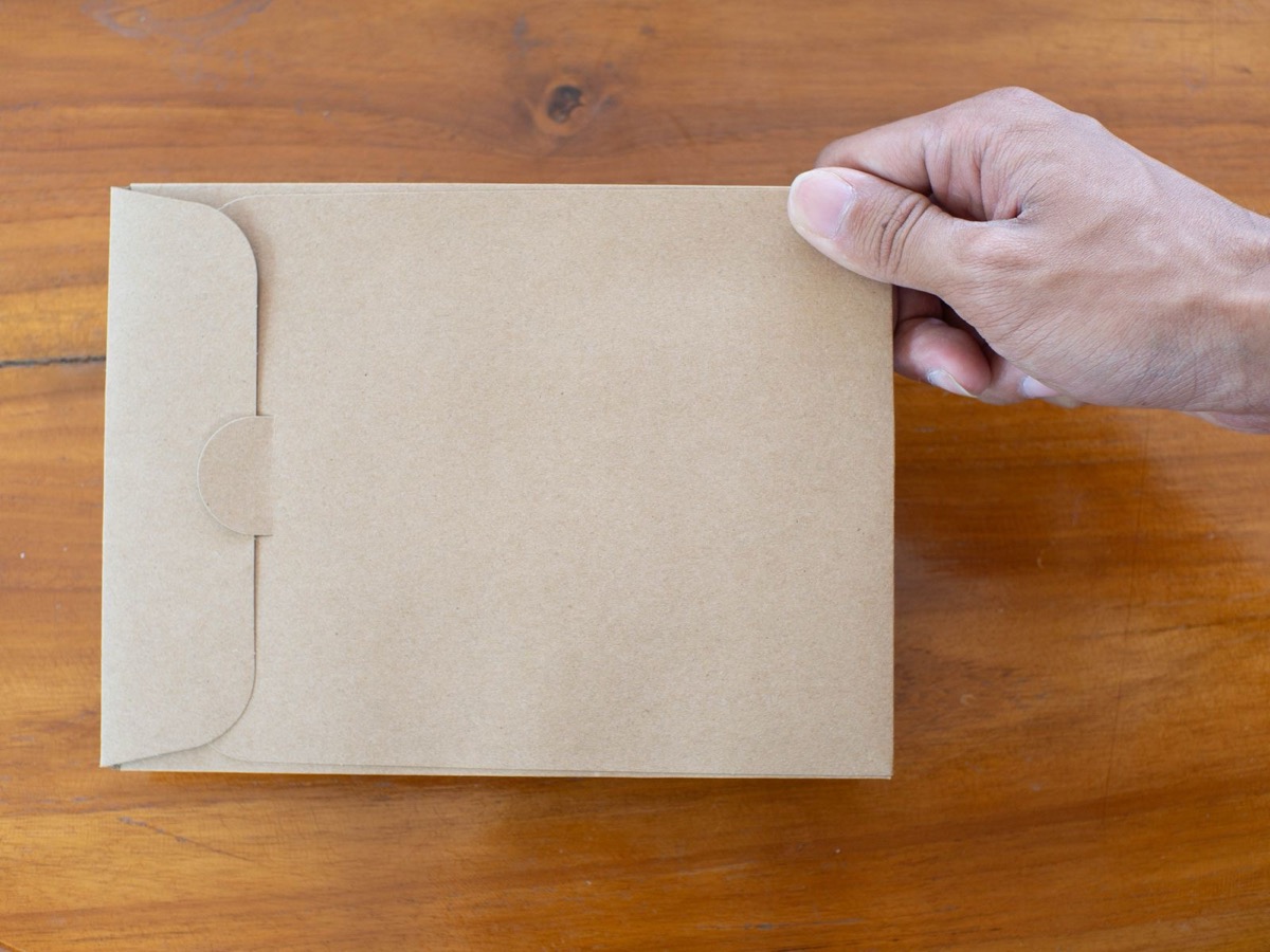 A hand holding a plain brown envelope on a wooden desk