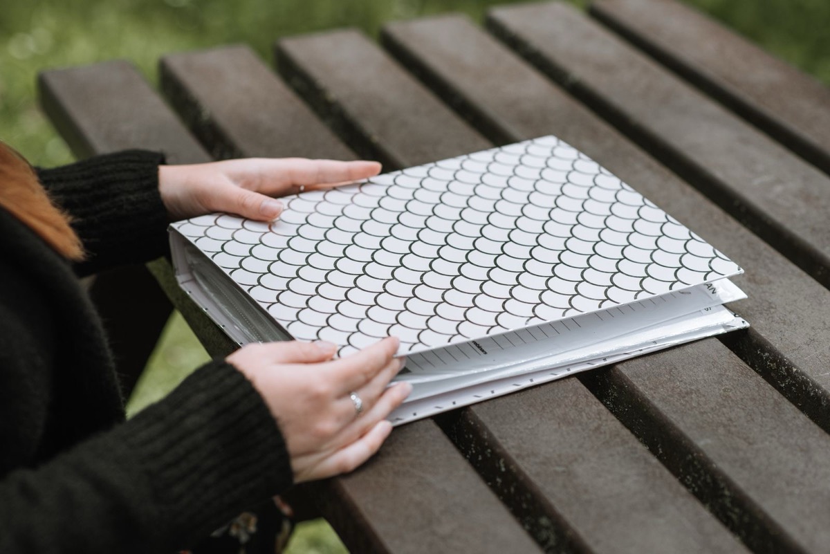 Two hands resting on a closed patterned ring binder on a wooden table