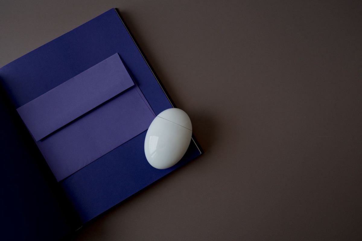 A closed blue folder with a lilac envelope and a white computer mouse on a dark grey desk