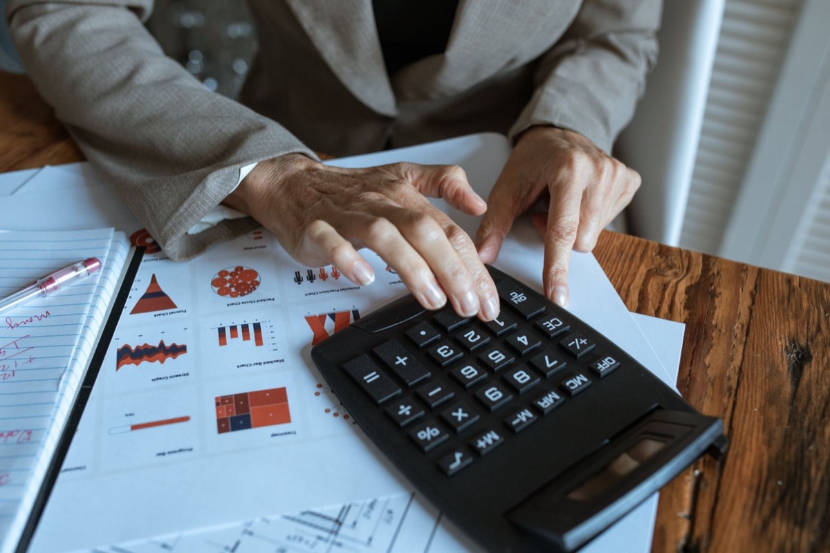 Hands on a black calculator over printed charts on a wooden desk