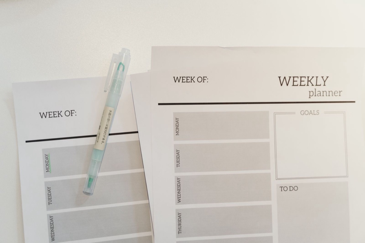 Two blank weekly planner sheets with a pale-green pen lying on top