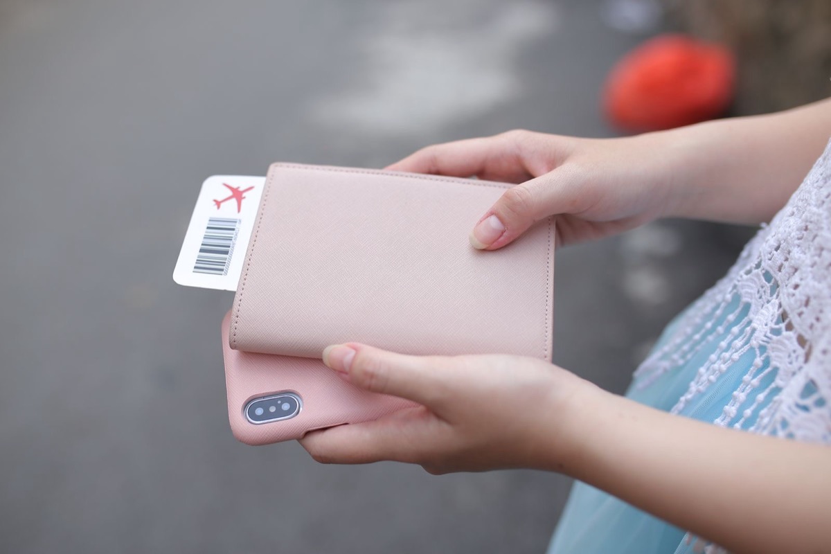Two hands holding a pink travel wallet with a boarding pass sticking out, above a phone in a pink case