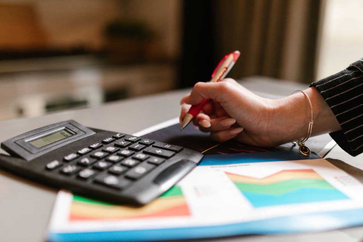 A hand with a red pen beside a calculator and printed colour charts on a desk