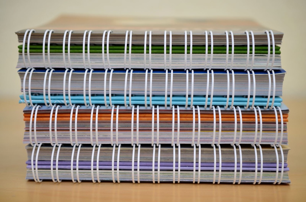 A stack of colourful spiral-bound notebooks on a wooden table