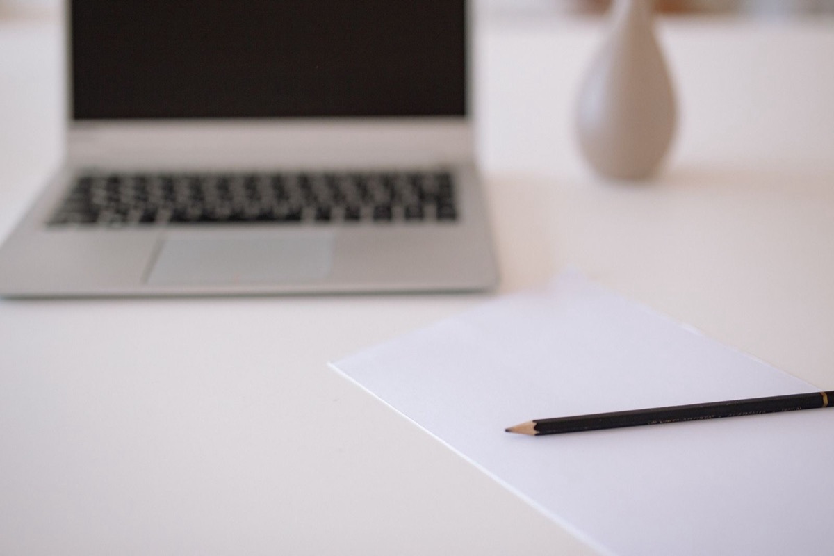 A laptop, a blank sheet of paper and a pencil on a white desk