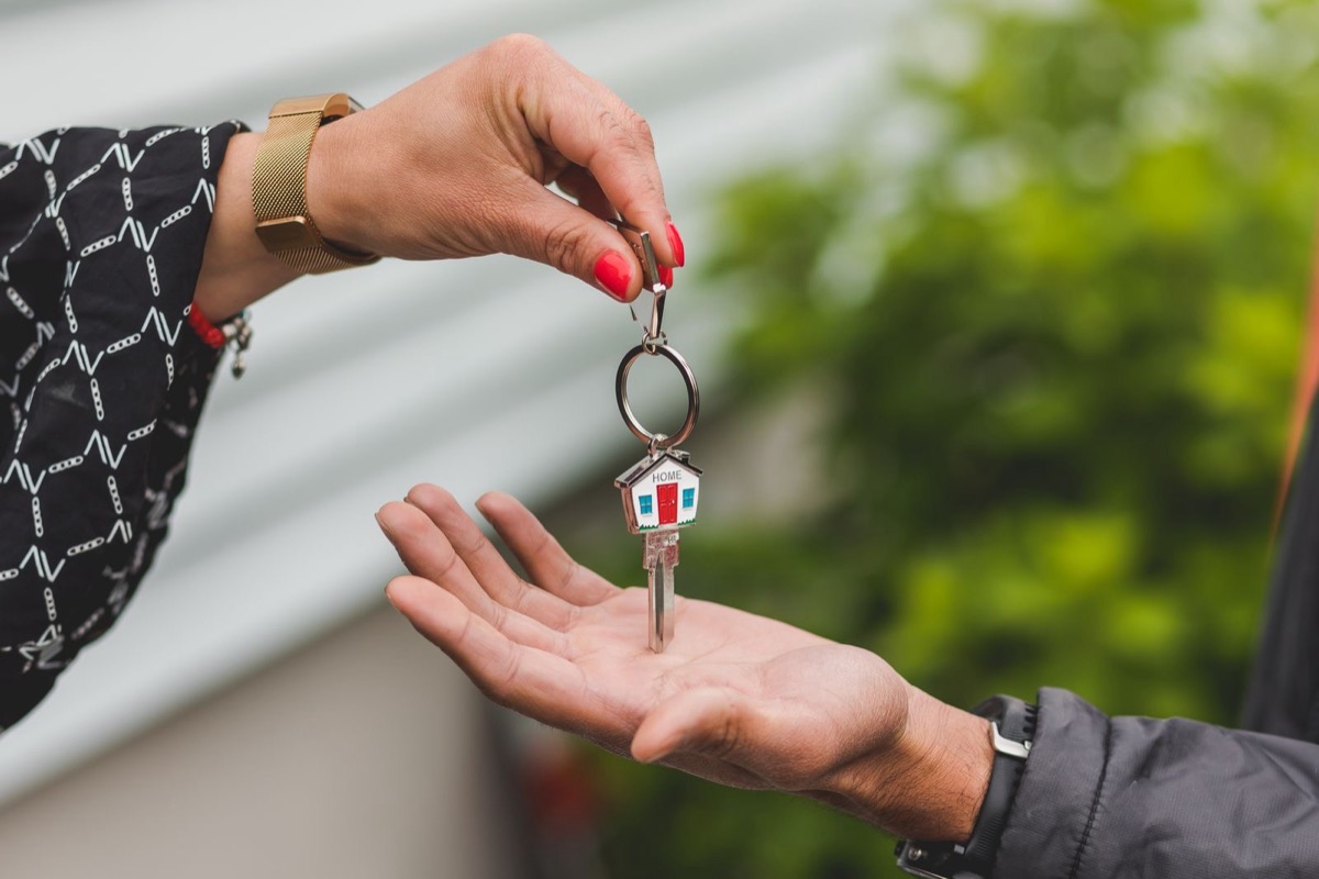 A hand passing a key on a house-shaped key ring into an open palm
