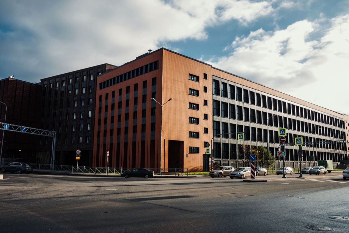 A brick office building on a street corner under a partly cloudy sky, with cars parked along the road