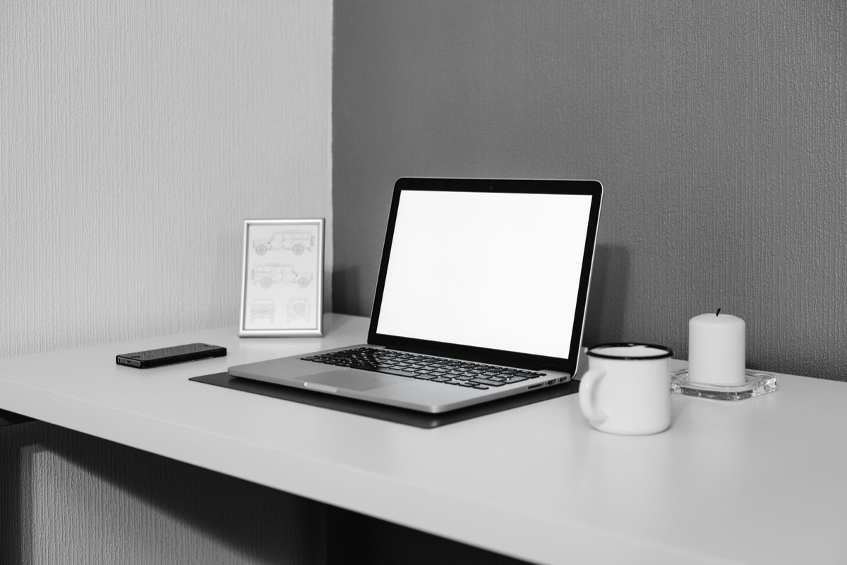 A laptop with a blank screen on a grey desk, with a framed picture, a mug and a candle