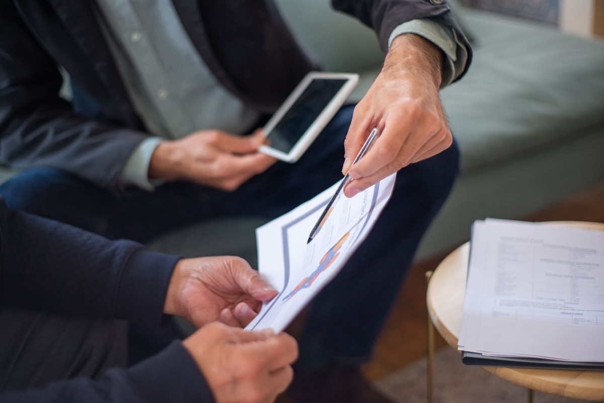 Two people's hands holding a printed sheet between them, one with a pen, and a tablet