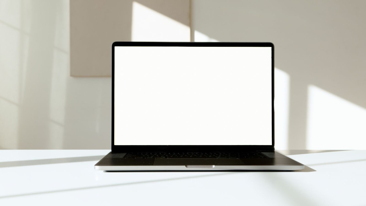 A laptop with a blank white screen on a white desk in daylight