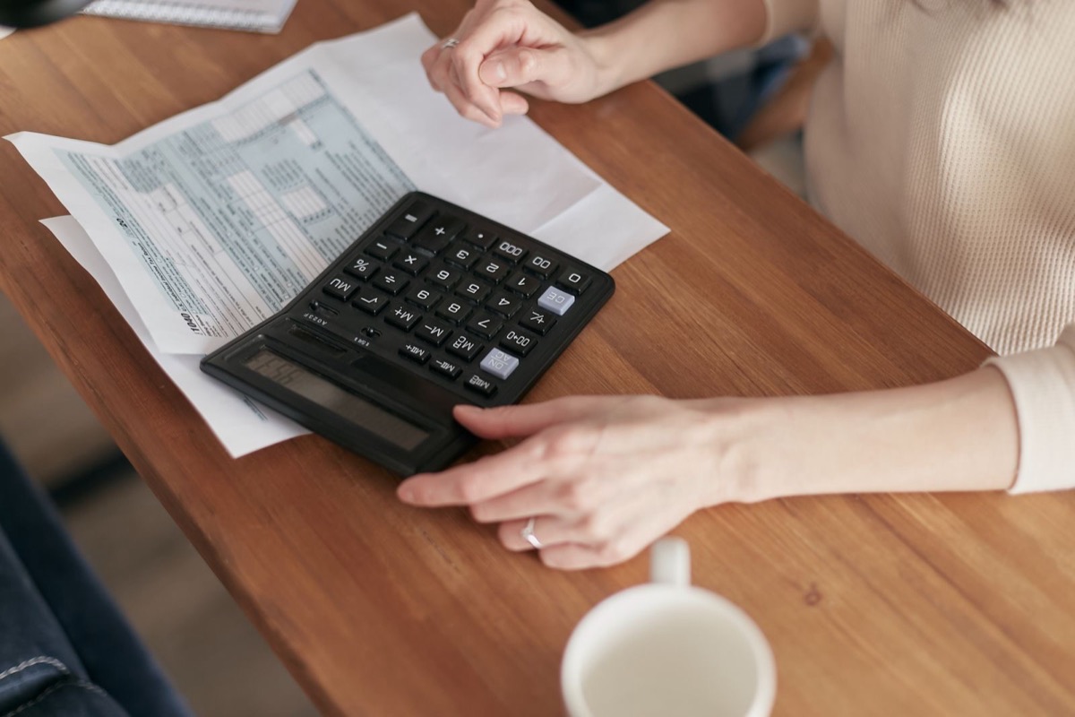 Hands on a calculator beside a printed form on a wooden desk